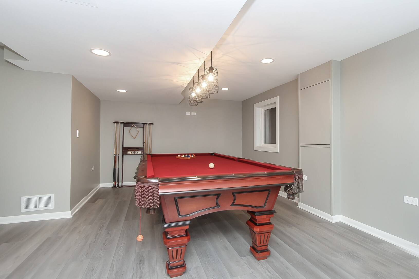 Gray Finished Basement With Red Billiards Table and Hanging Light Fixtures Above