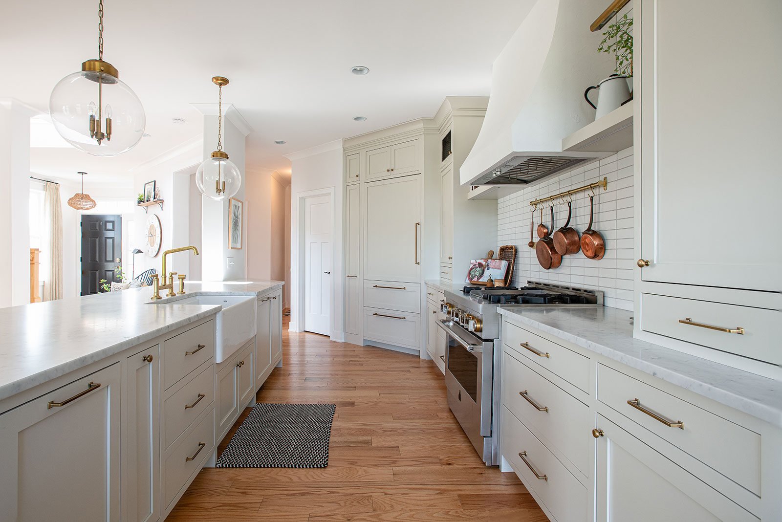 Custom white kitchen renovation featuring an efficient work triangle, marble-topped island, apron sink, and stainless steel range.