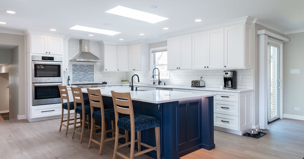 Custom kitchen layout showing a navy blue island with bar seating that buffers the main work triangle and wall ovens from guest traffic.